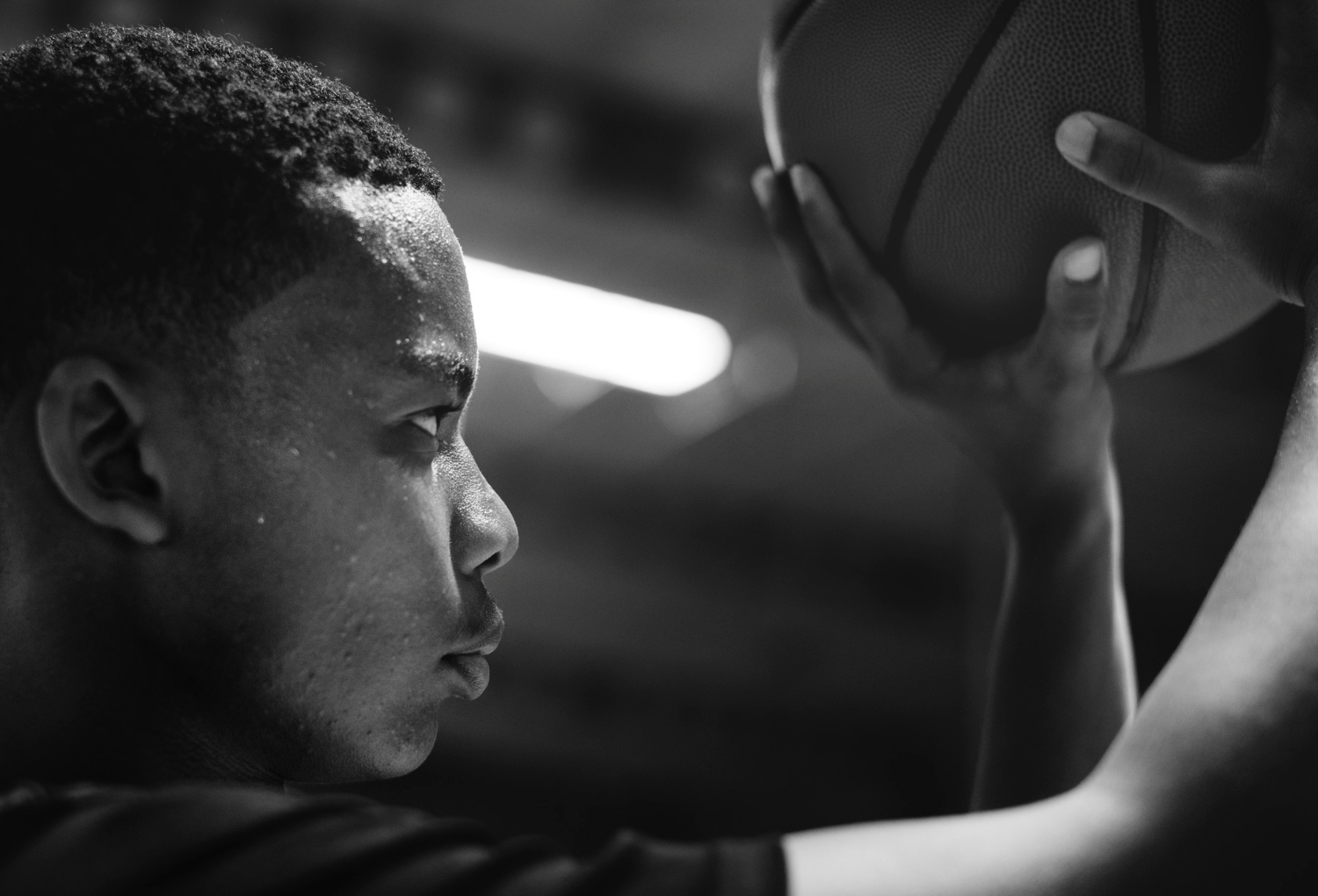 Close-up black and white photo of a focused young man holding a basketball, preparing to shoot.