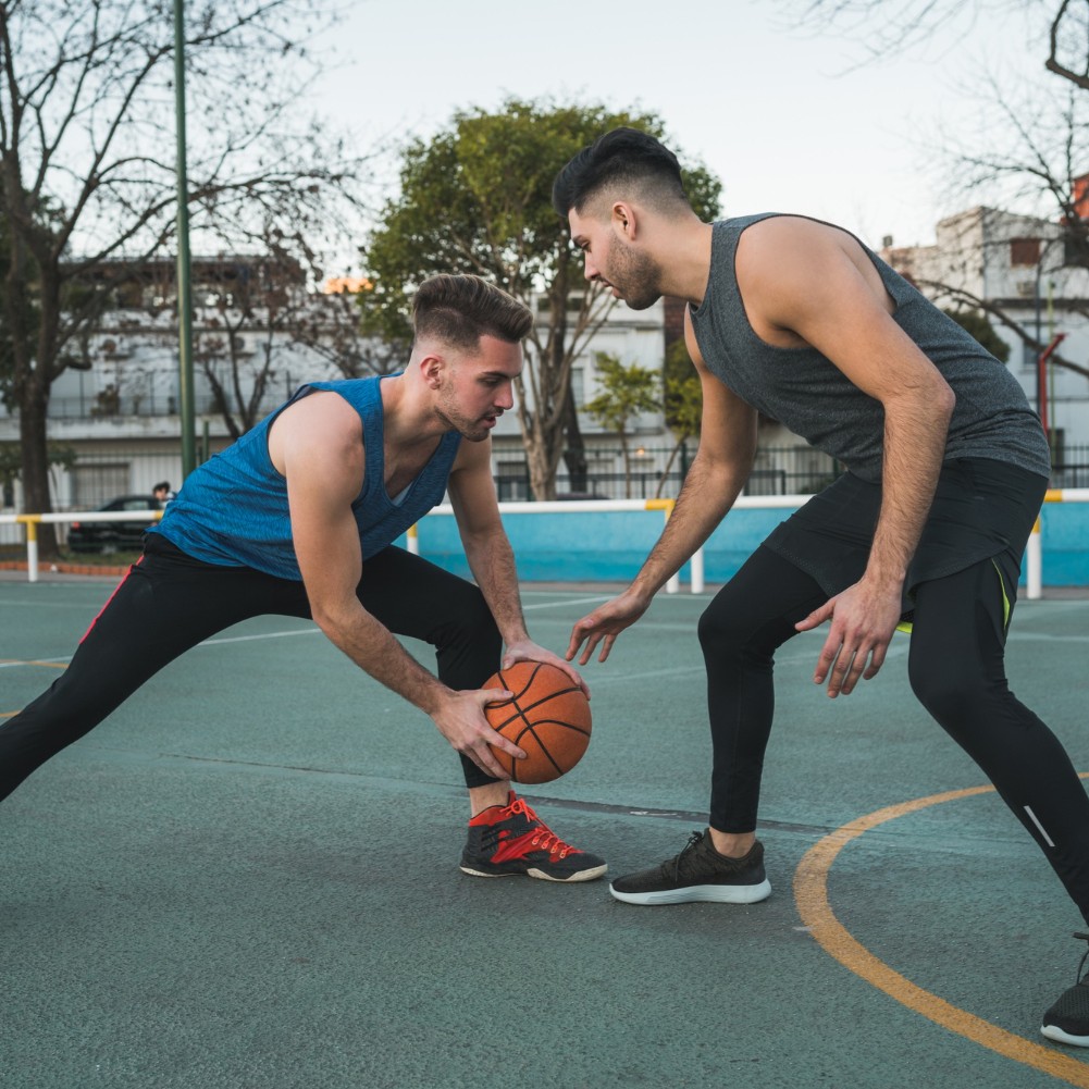 Two men playing basketball outdoors, one dribbling the ball while the other defends.