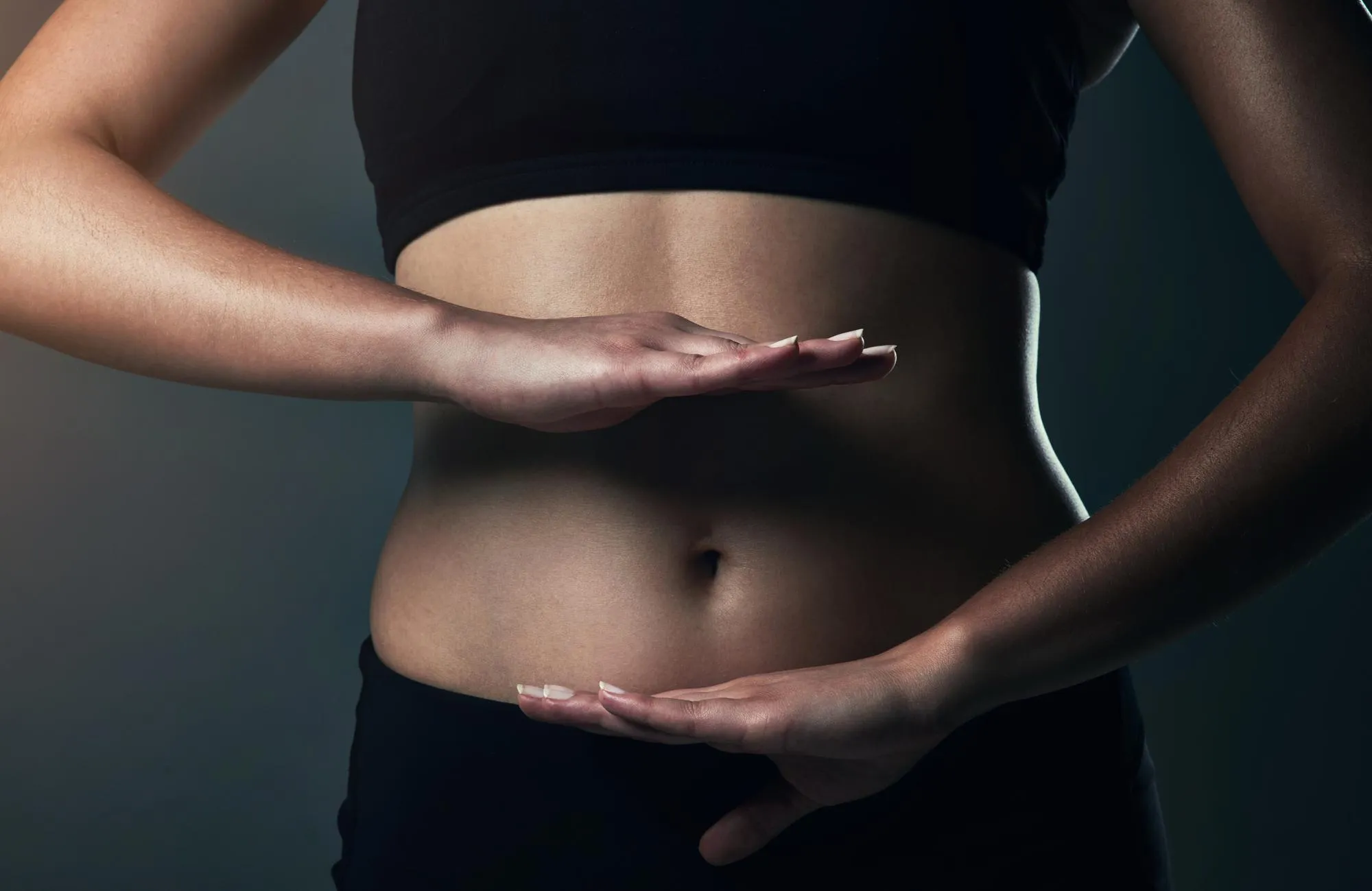 Close-up of a woman's toned midsection with hands framing the stomach area.