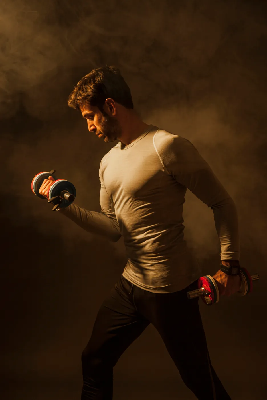 Man lifting dumbbells with focused expression in smoky gym lighting.