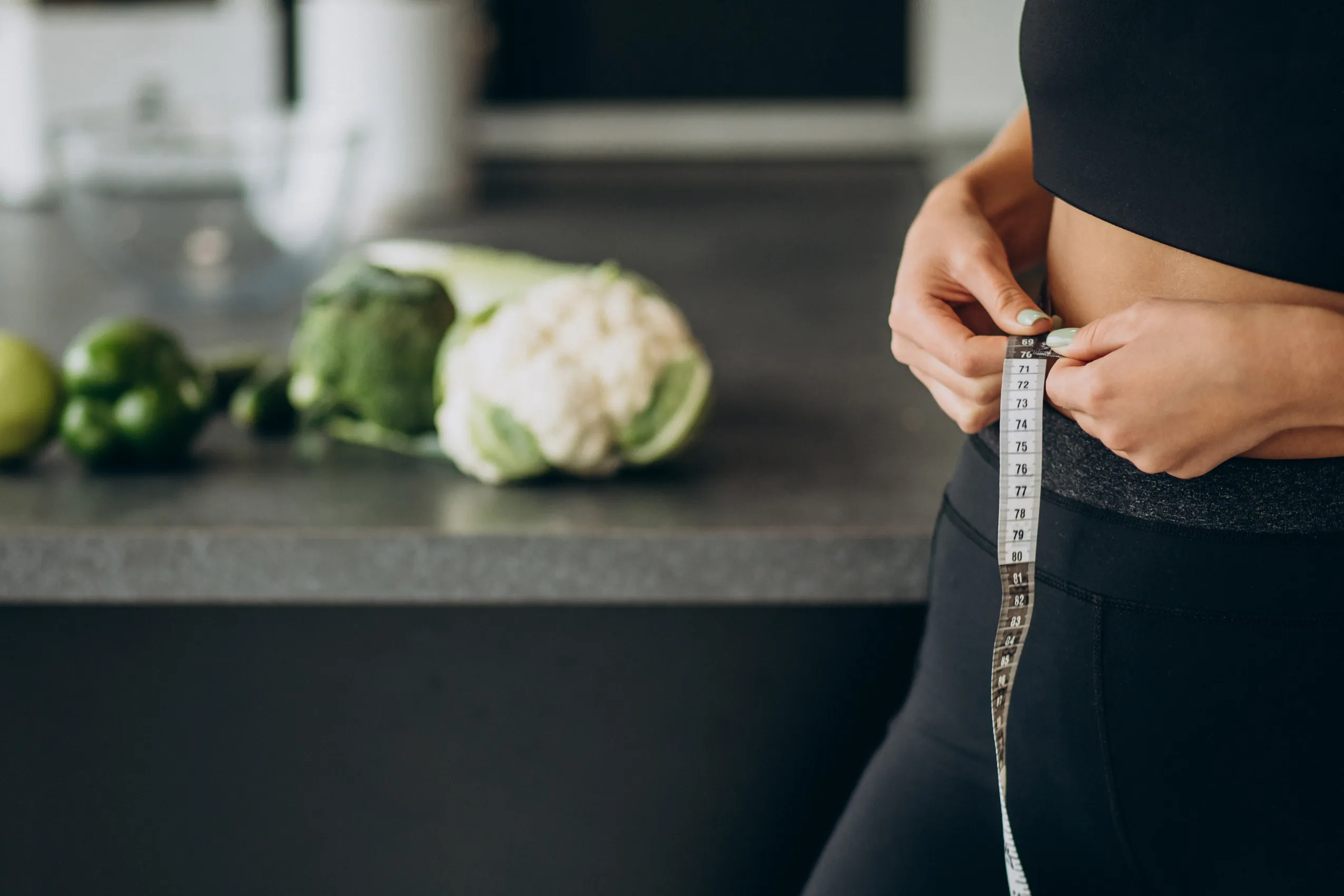 Person in black workout clothes measuring their waist with a white and black tape measure.