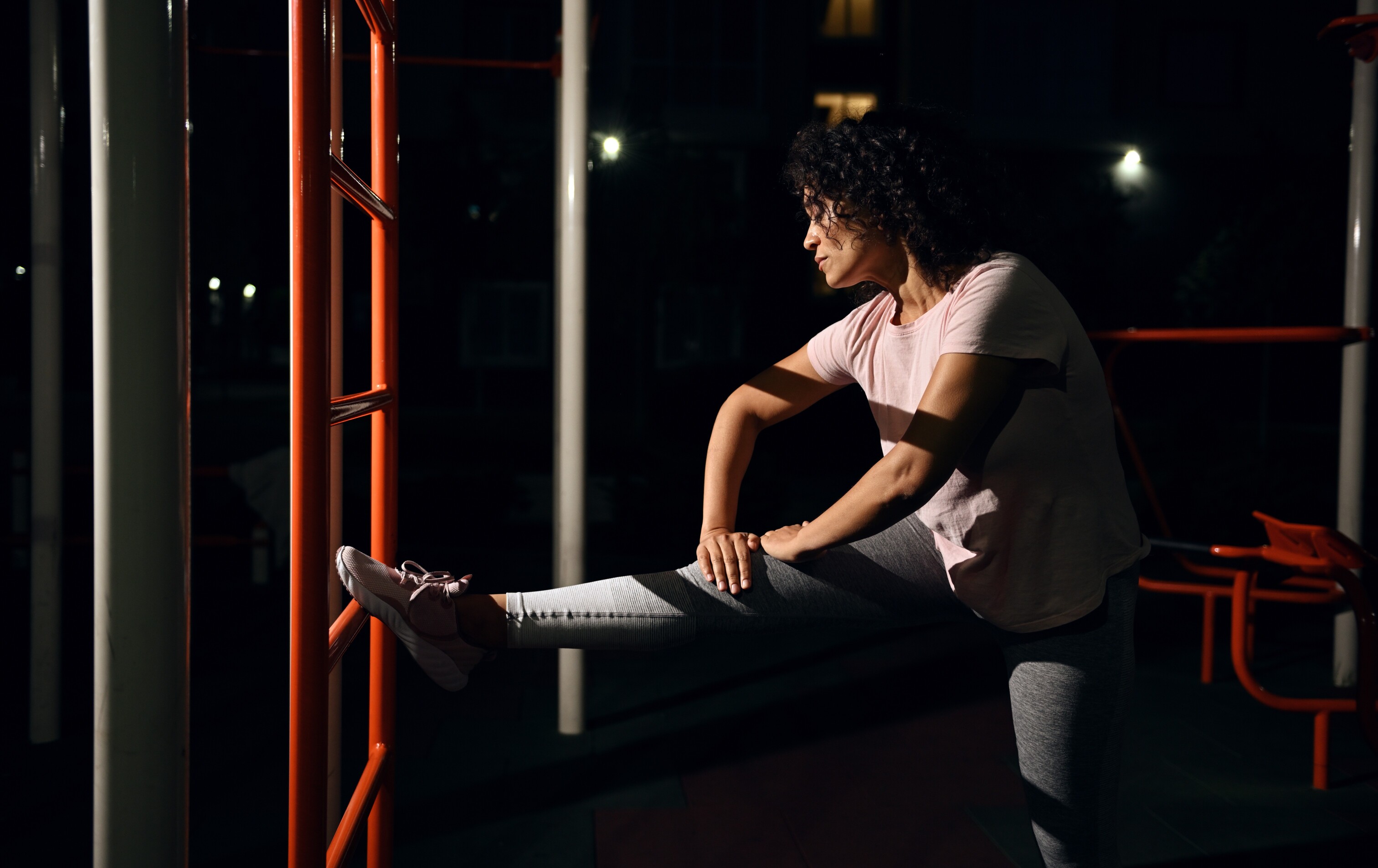 Woman stretching her leg on an orange exercise ladder at night in an outdoor gym.