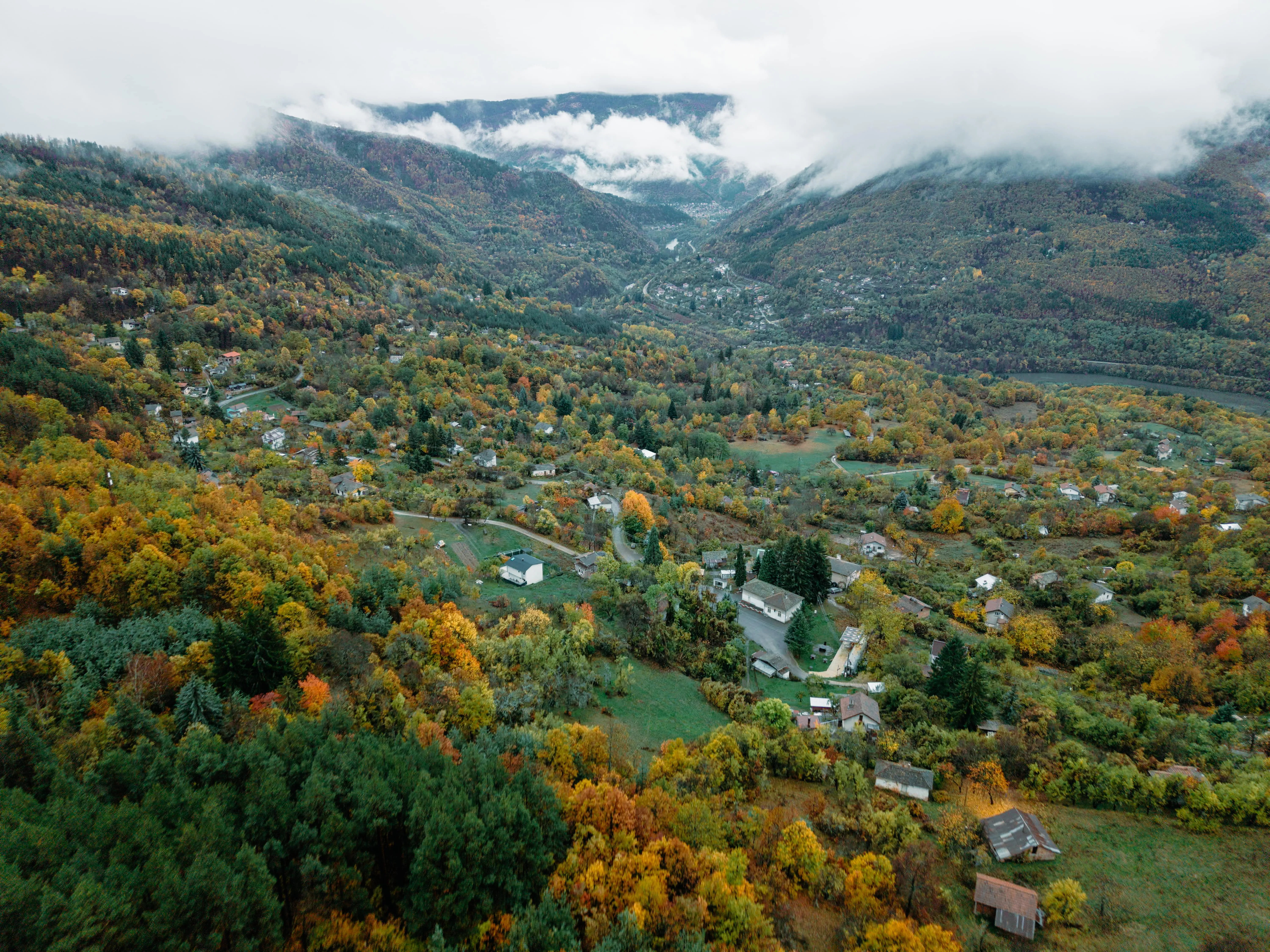 Drone shot of fog drifting over a densely forested mountain range.