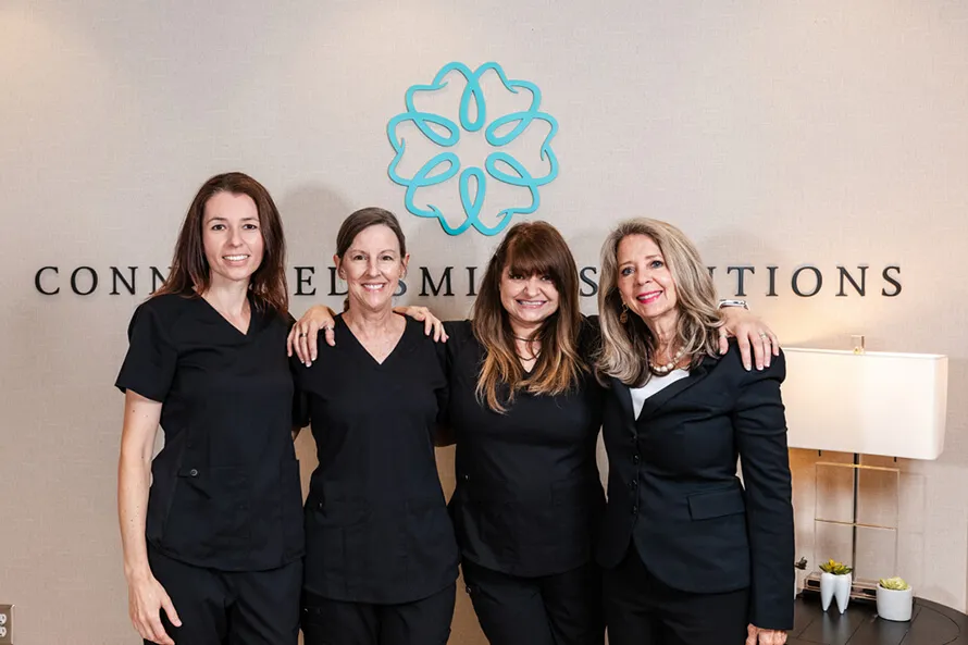Four Connected Smile Solutions staff members standing at the front desk and smiling.