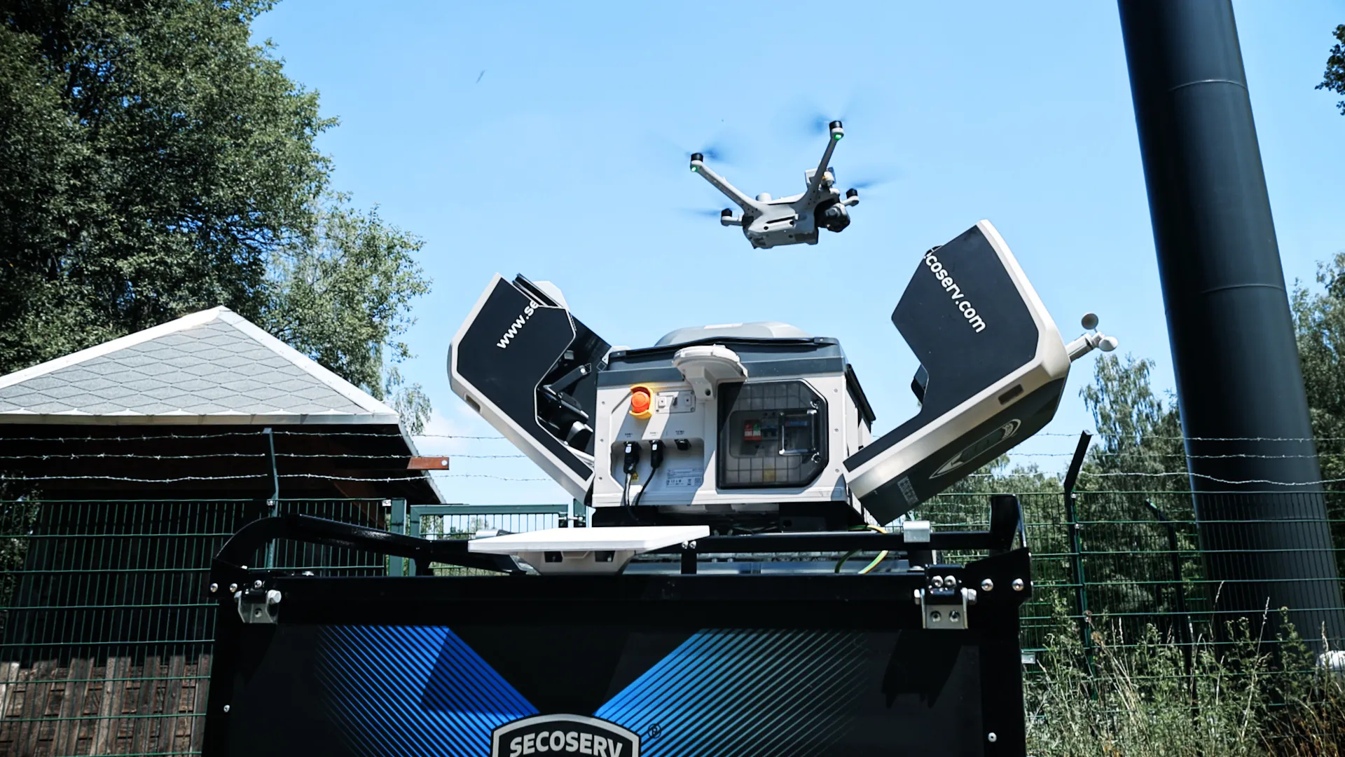 Eine Drohne fliegt über einem offenen, schwarzen und blauen SECOserv-Gerät im Freien vor einem blauen Himmel mit Bäumen im Hintergrund.