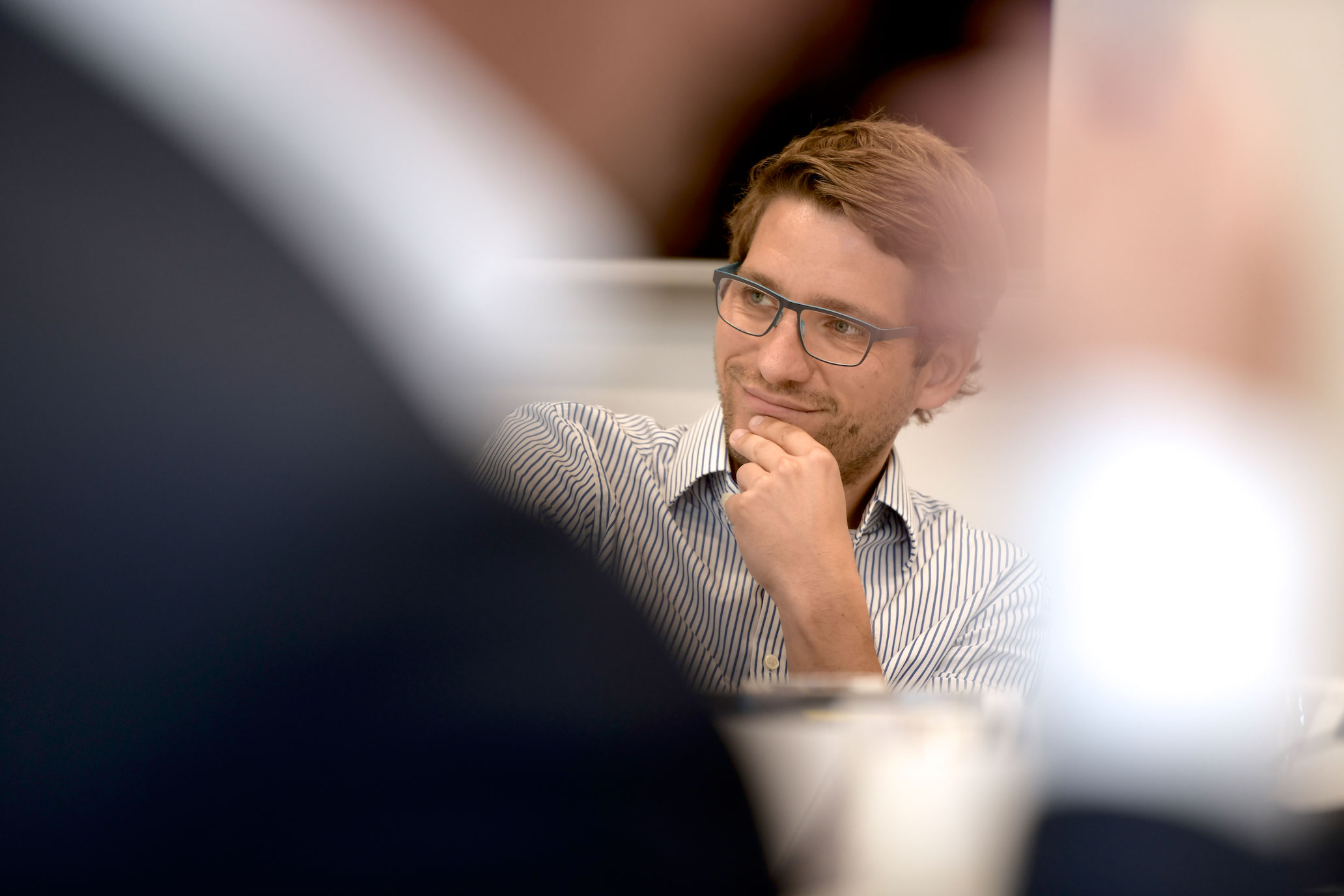 Portrait von Journalist Cliff Lehnen, wie er mit einem gestreiften Hemd an einem Konferenztisch sitzt