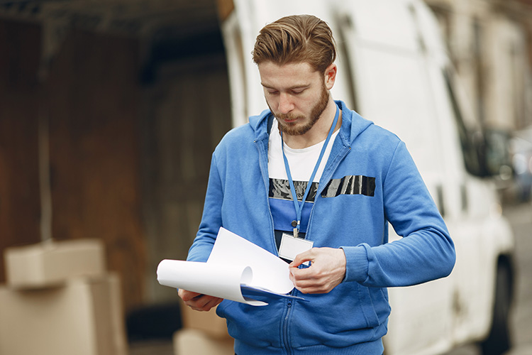 Delivery worker checking documents in front of a van with shipping boxes for last-mile logistics