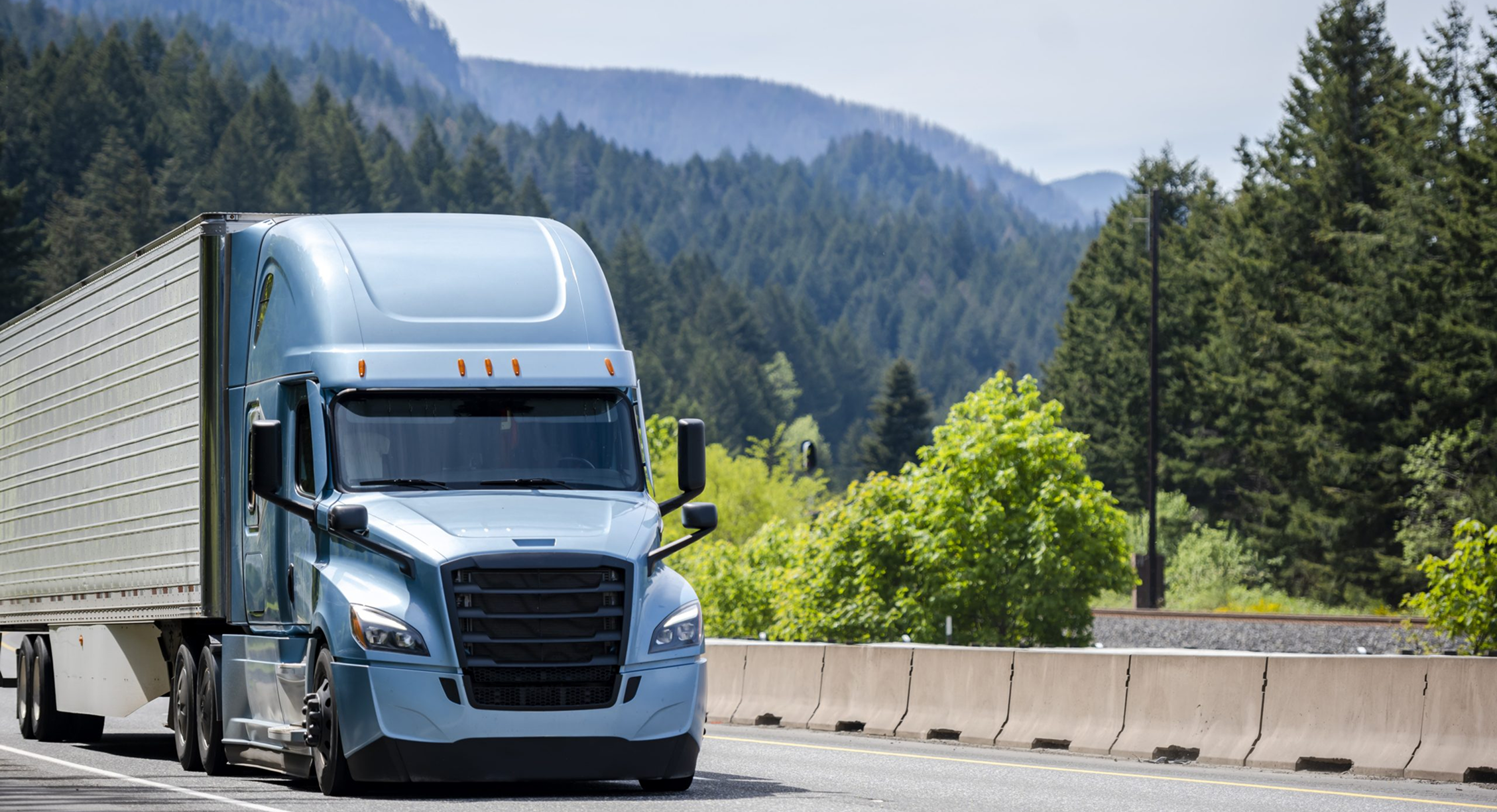 Blue semi-truck hauling trailer on highway through forested mountains representing long-haul freight transportation