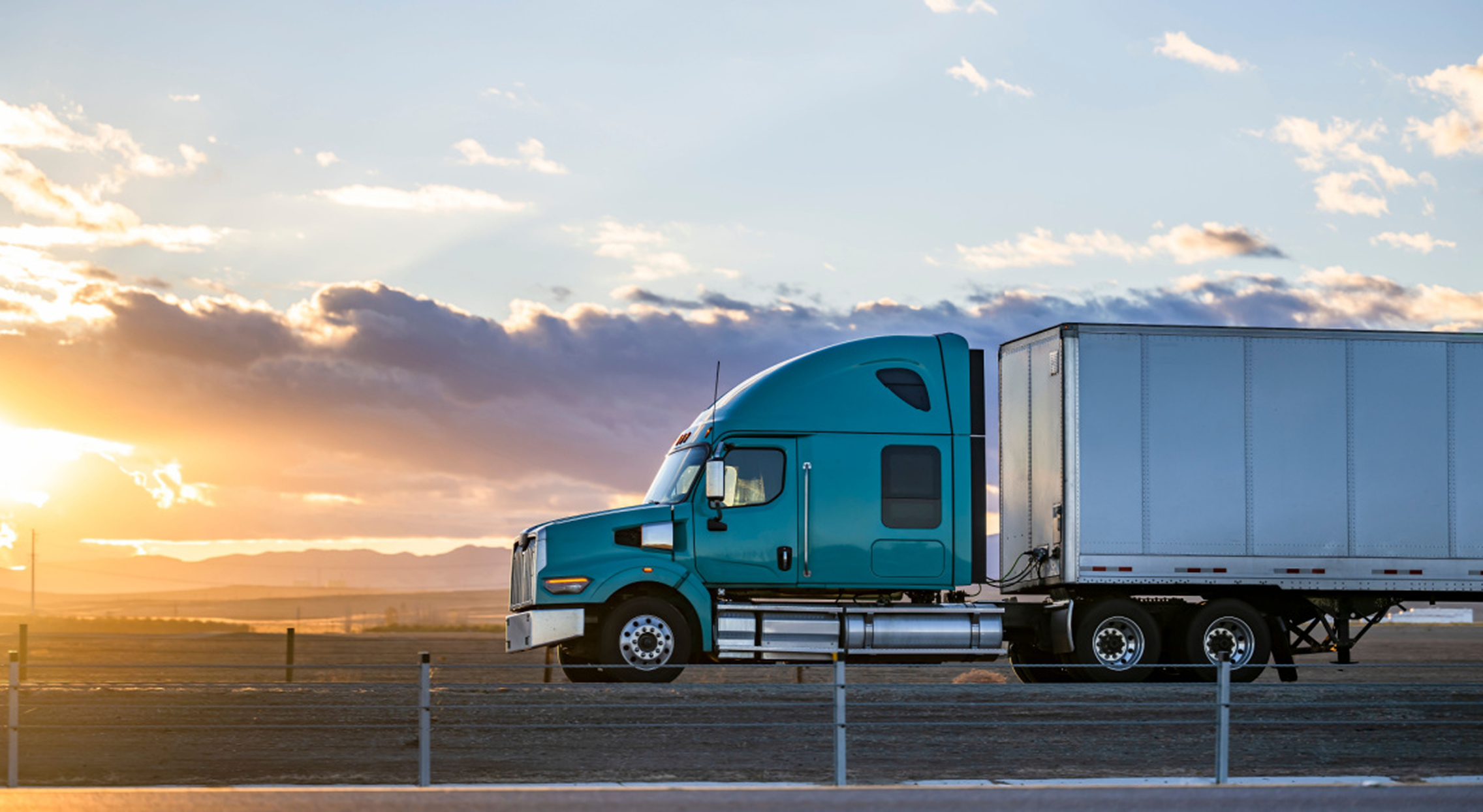 Teal semi-truck with trailer driving at sunset representing nationwide freight transportation