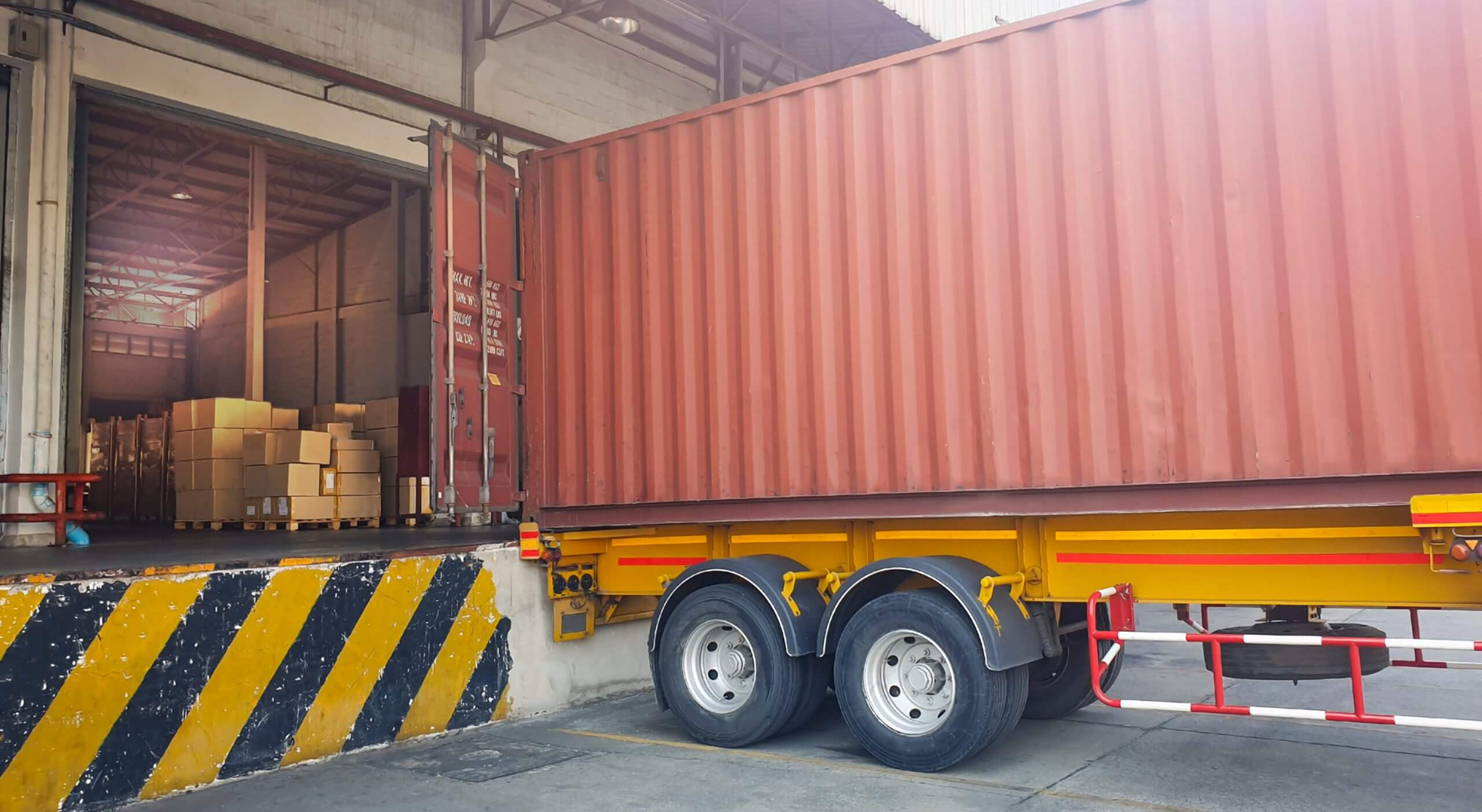 Shipping container truck unloading cardboard boxes at warehouse dock for freight logistics