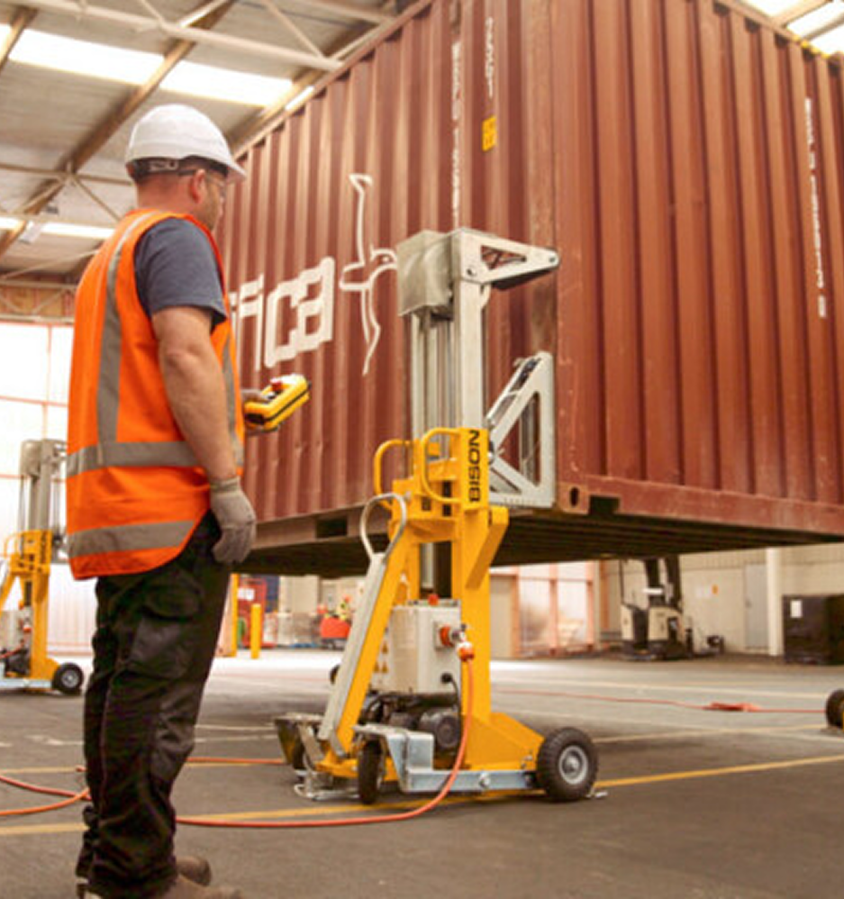 Logistics worker in safety vest operating equipment to load full shipping container at warehouse