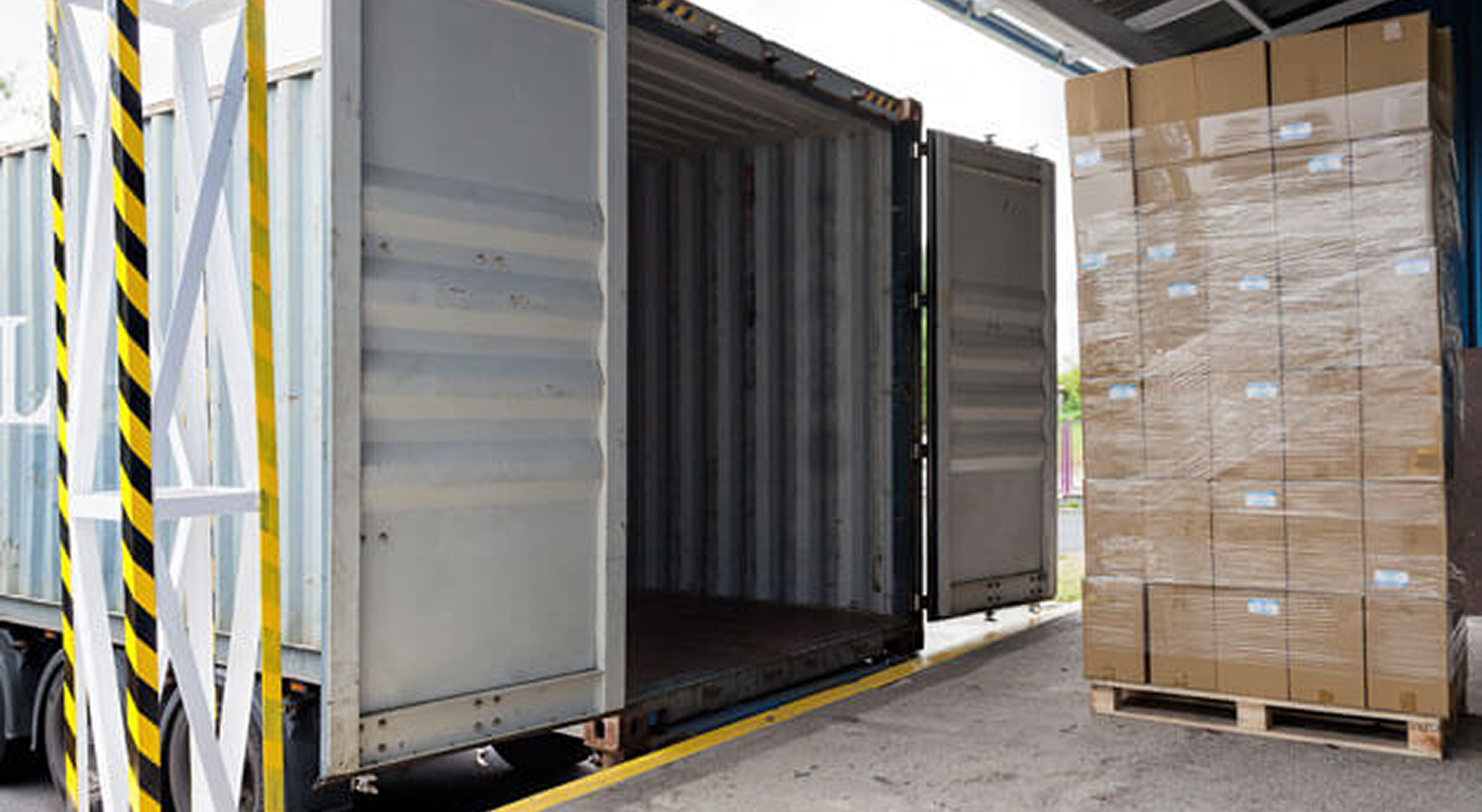 Shipping container at warehouse with palletized cardboard boxes ready for loading