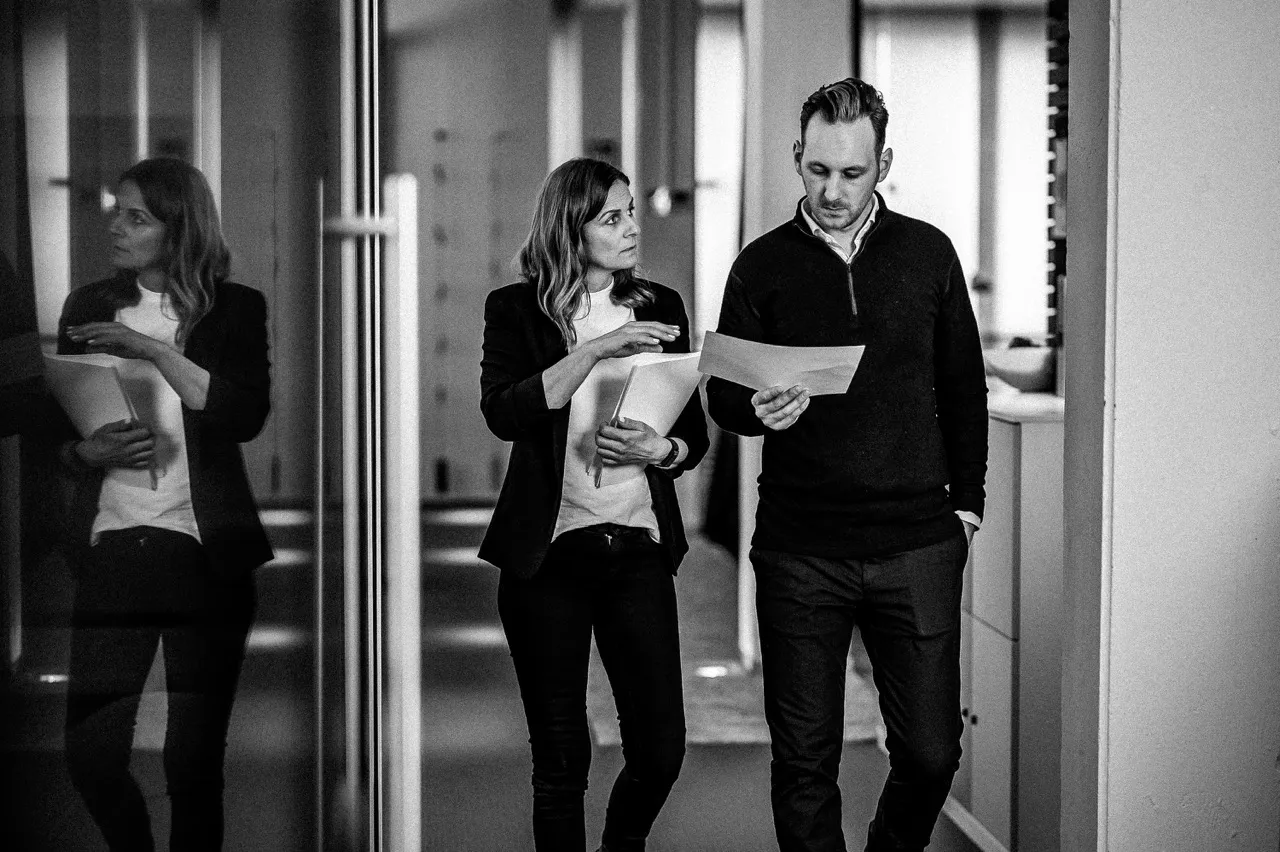 Pierre Fey und Tanja Fey – Geschäftsführer und Geschäftsführerin von Fey Consulting, Experte für Unternehmensberatung auf einem Flur laufend, Besprechungssituation mit Papier in der Hand