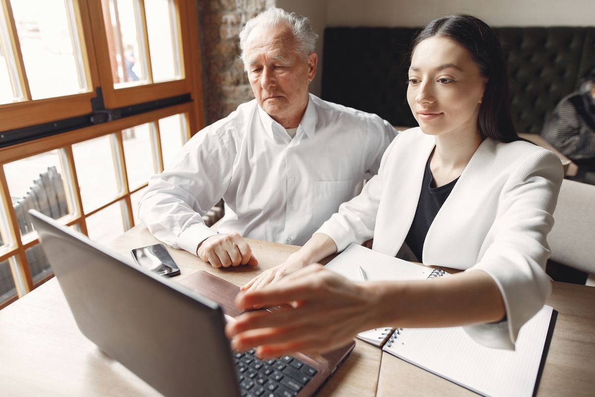 Woman showing an older man something on a laptop at a table