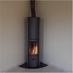 Modern black cylindrical wood-burning stove with visible flames, installed in a corner on tiled floor.