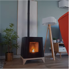 Modern living room corner with a black wood-burning stove emitting firelight, a tall indoor plant in a brown pot, a wooden tripod floor lamp with a white shade, and a partial view of red furniture on wooden flooring.