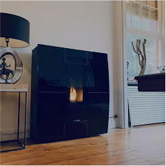 Modern minimalist living room corner with a sleek black fireplace on a wooden floor, a round wall clock with a black frame, and a black lamp on a side table, next to a large window with white blinds and a decorative branch sculpture on the windowsill.
