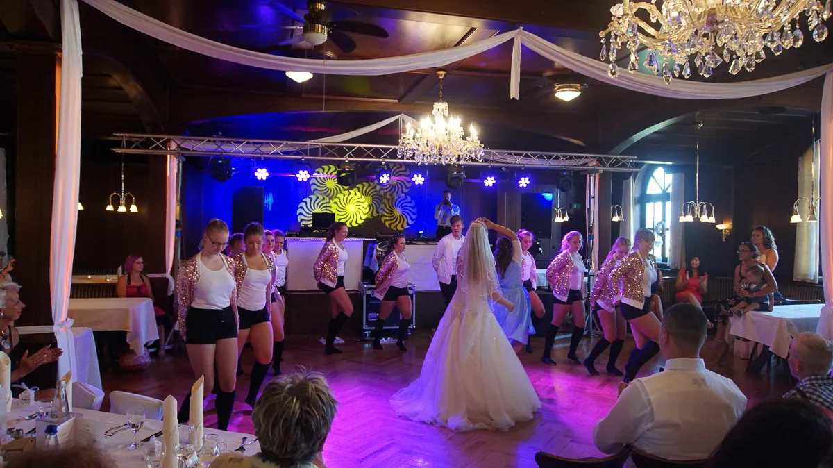 Hochzeitspaar tanzt vor der Bühne mit Showtanzgruppe – DJ Hädwig sorgt für Musik und Lichtstimmung in edler Location.