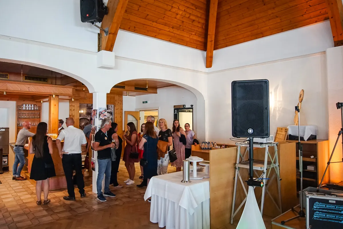 Geselliger Empfang im Eingangsbereich – Gäste unterhalten sich an der Bar und im Vorraum des Festsaals, im Vordergrund Lautsprecher und Technik-Setup.