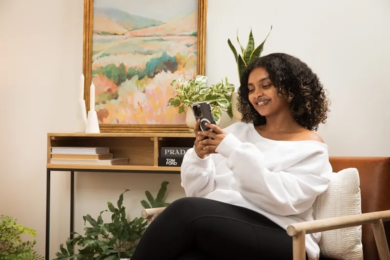 Woman relaxing at home, smiling while texting on her phone