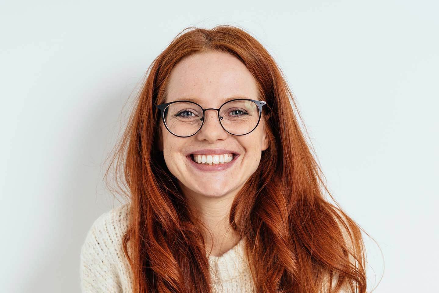A woman with red hair and glasses smiling.