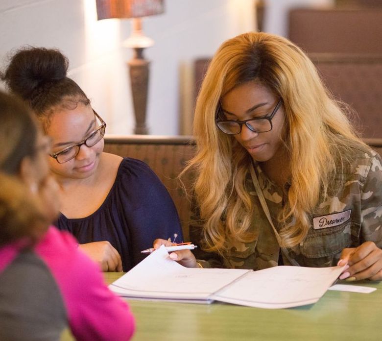 Three students gather around a table, reading from a worksheet.