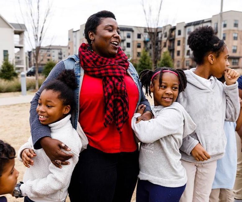 A woman and her daughters laugh while embracing.