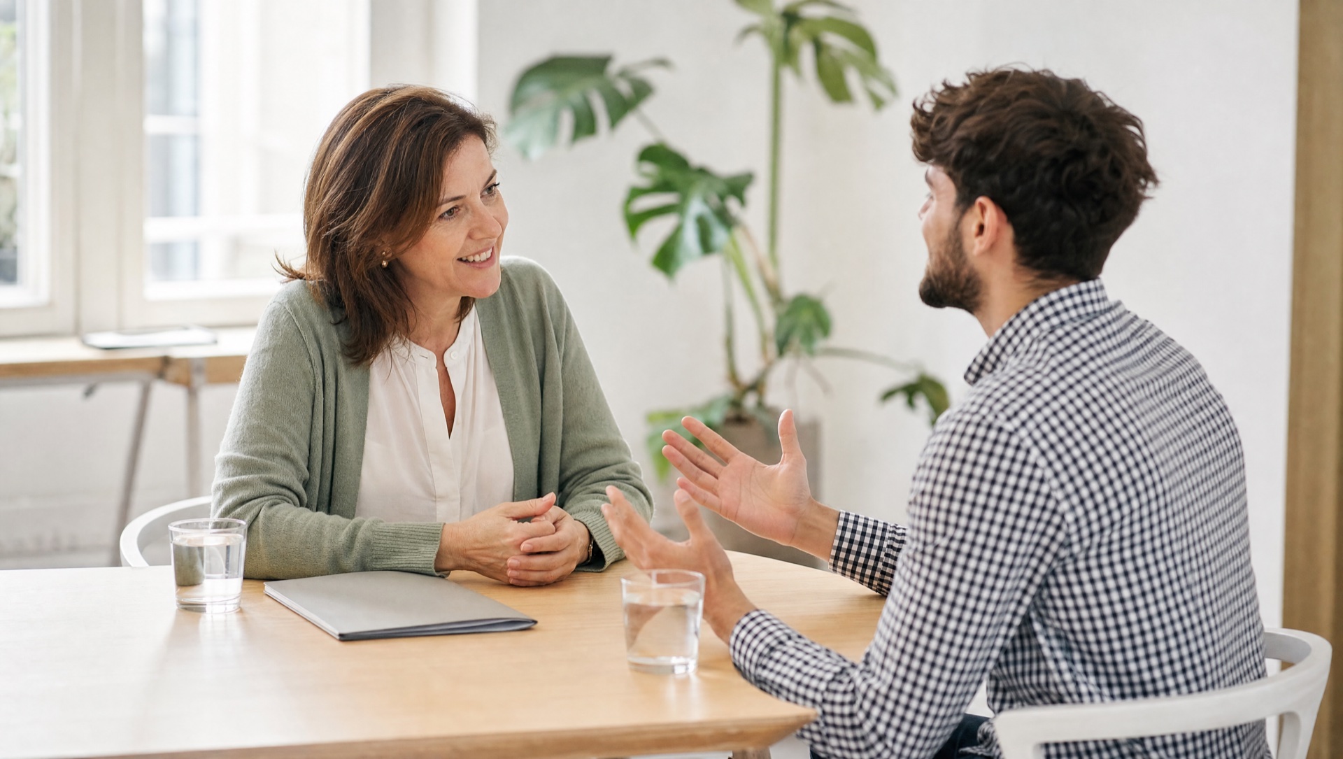 Ein Bewerbungsgespräch in einem hellen Besprechungsraum: eine Personalverantwortliche hört einem Bewerber zu