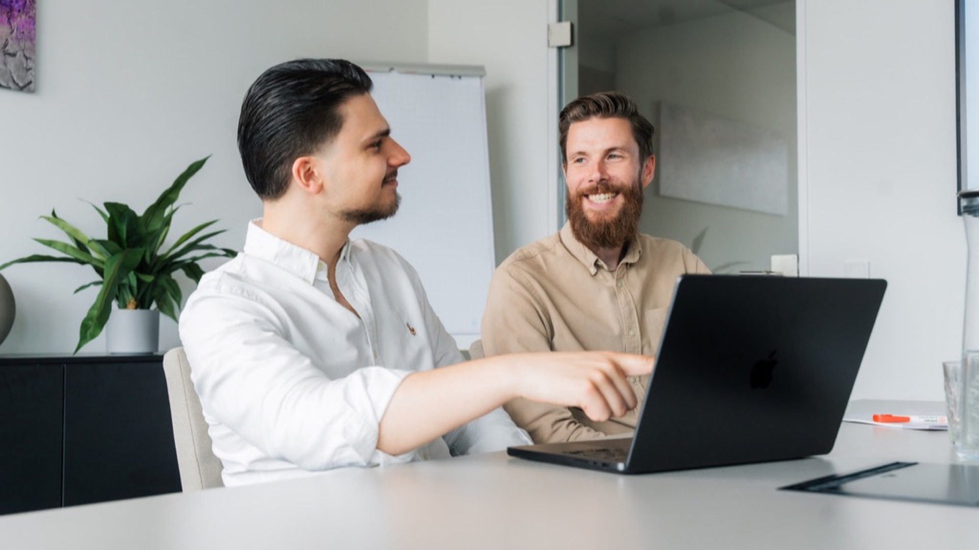 Zwei Kollegen besprechen an einem Laptop im hellen Besprechungsraum das Vorgehen bei der Personalgewinnung