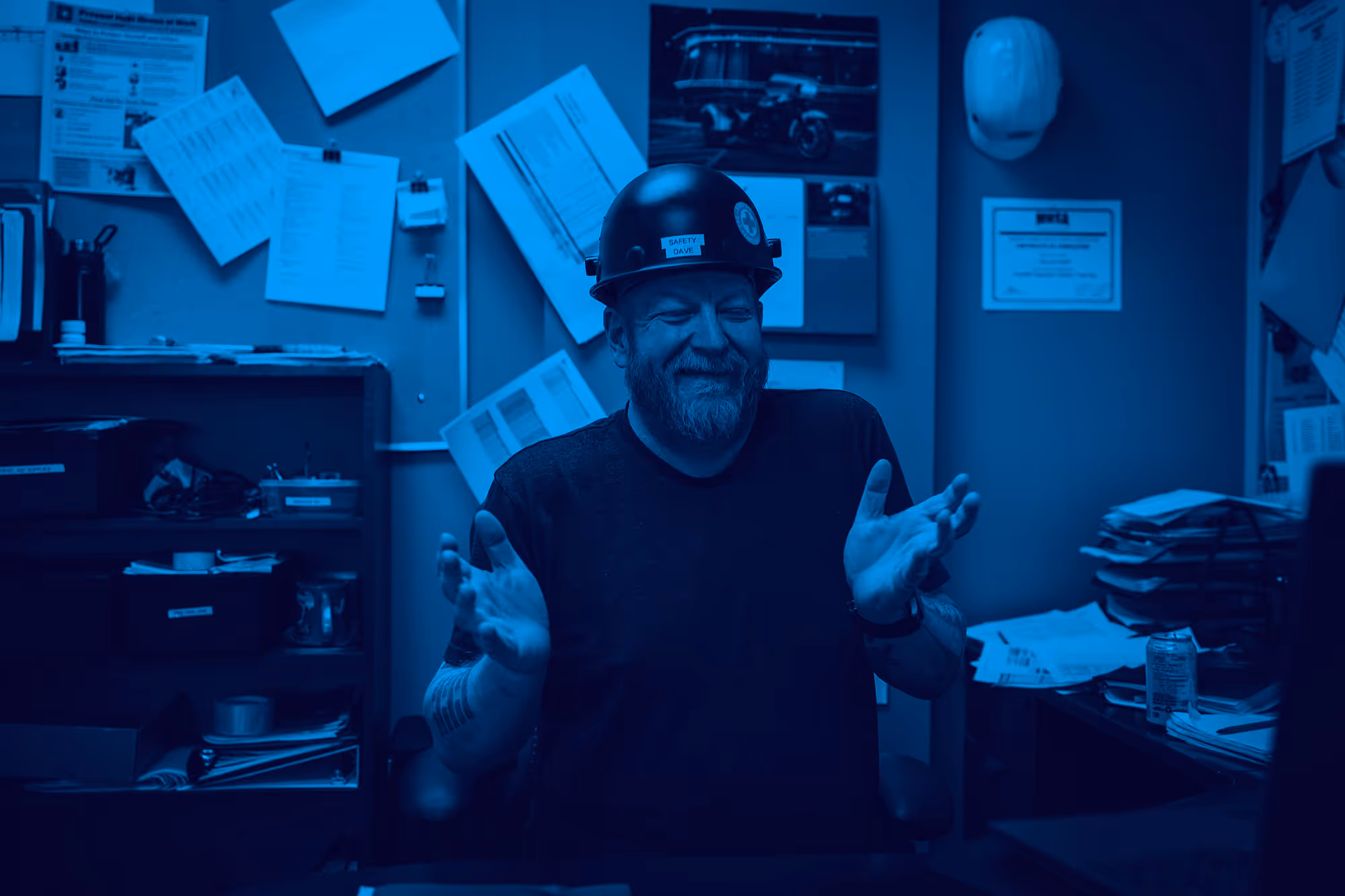 Smiling worker in hard hat gestures in blue-tinted industrial office