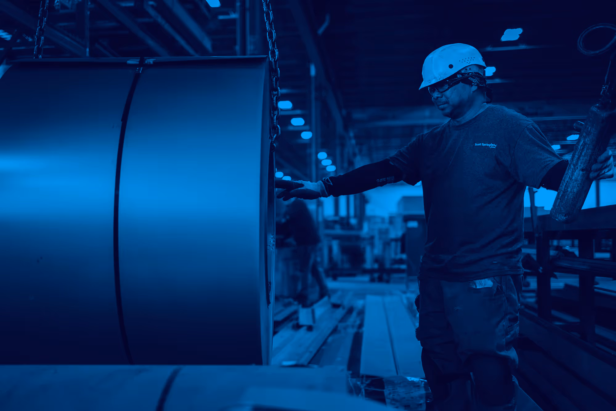 Worker in hard hat inspects large industrial machinery in blue-tinted factory