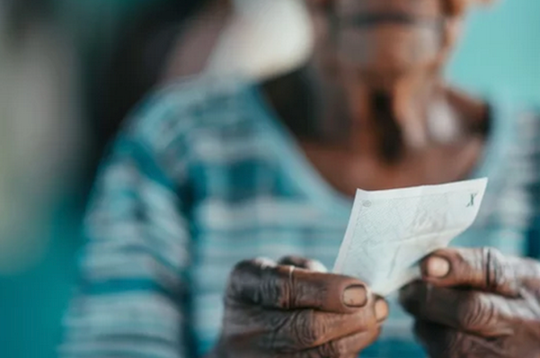 Elderly person holding a small piece of paper or document with both hands.