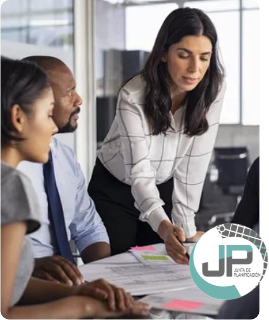 Businesswoman in a white checkered shirt leaning over a table discussing documents with colleagues in a modern office.