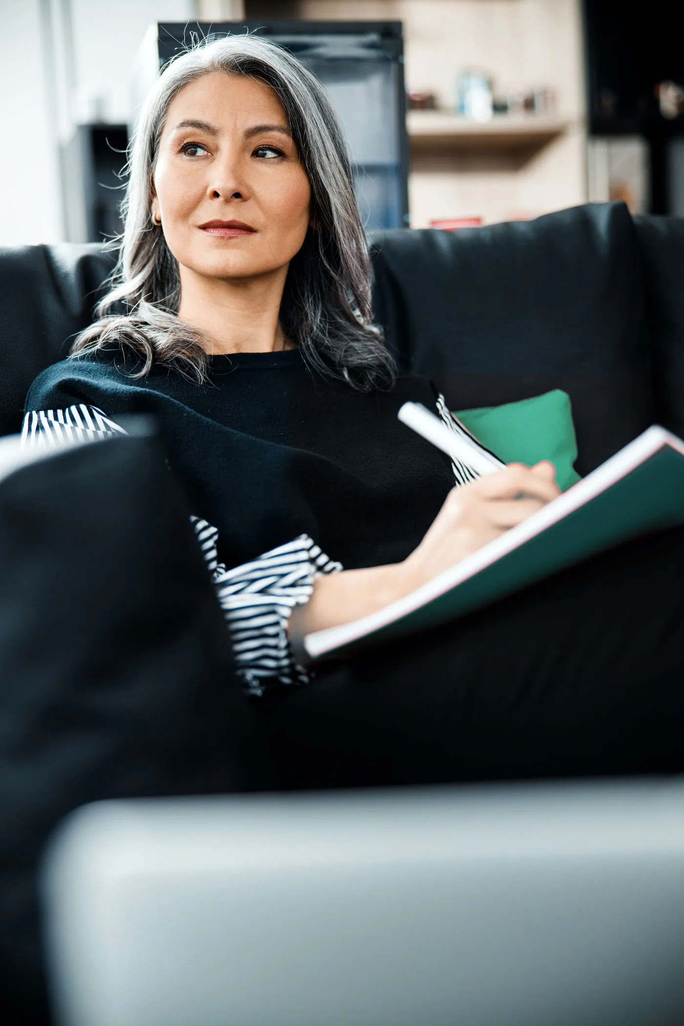 A woman sitting on a couch with a notebook, engrossed in her work and surrounded by a cozy atmosphere.