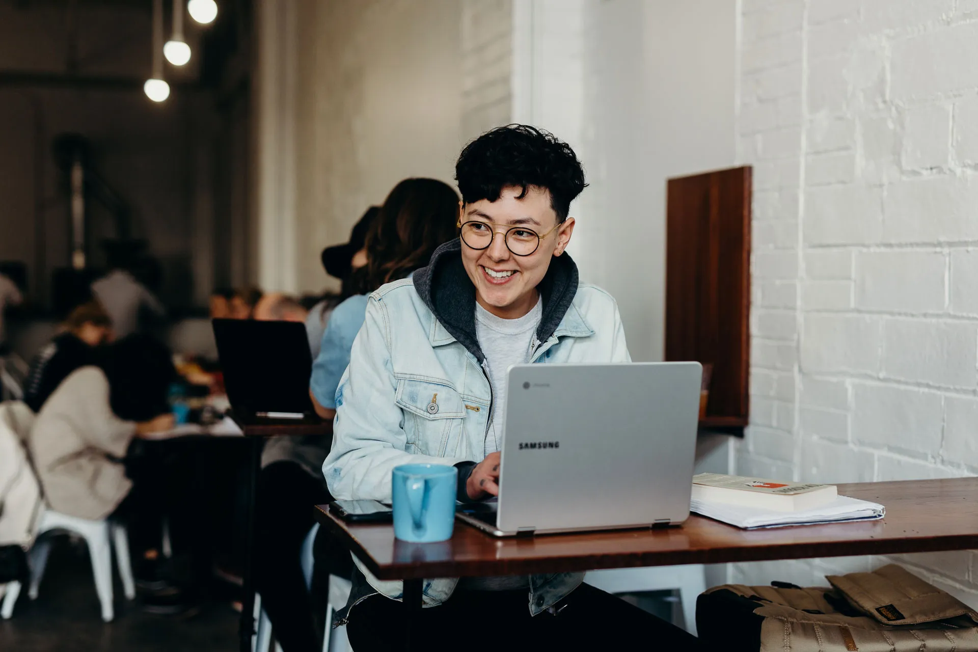 A person smiling while working on a laptop in a trendy café.