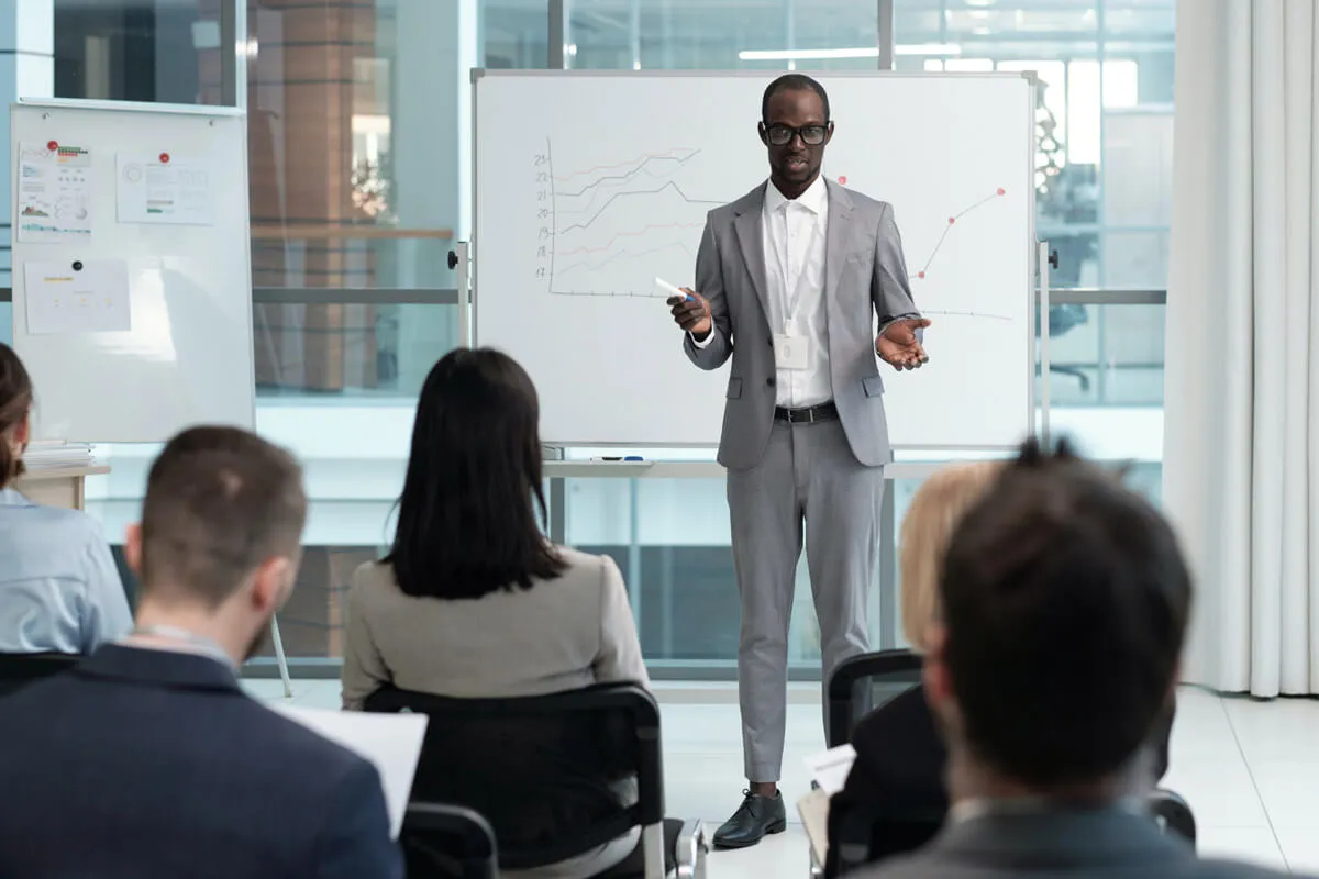 A man in a suit presenting to a group of people in a conference room.