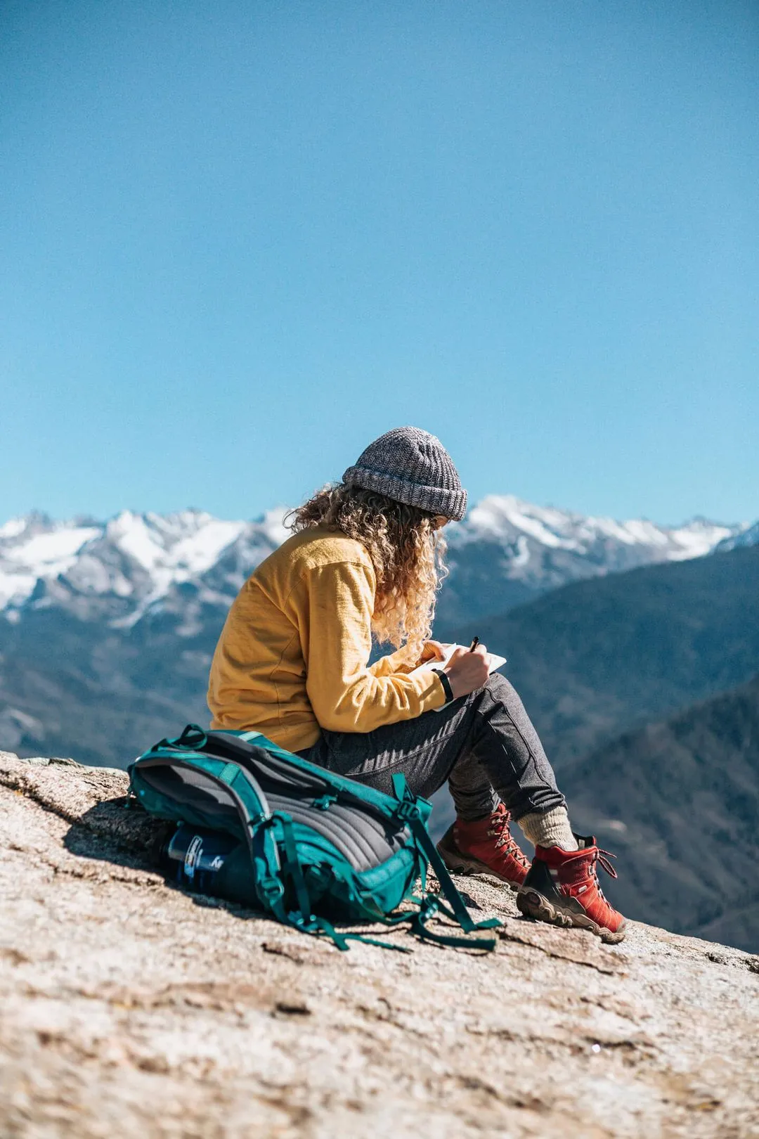 A woman sitting on a rock with her backpack, enjoying the scenic view of the mountains.