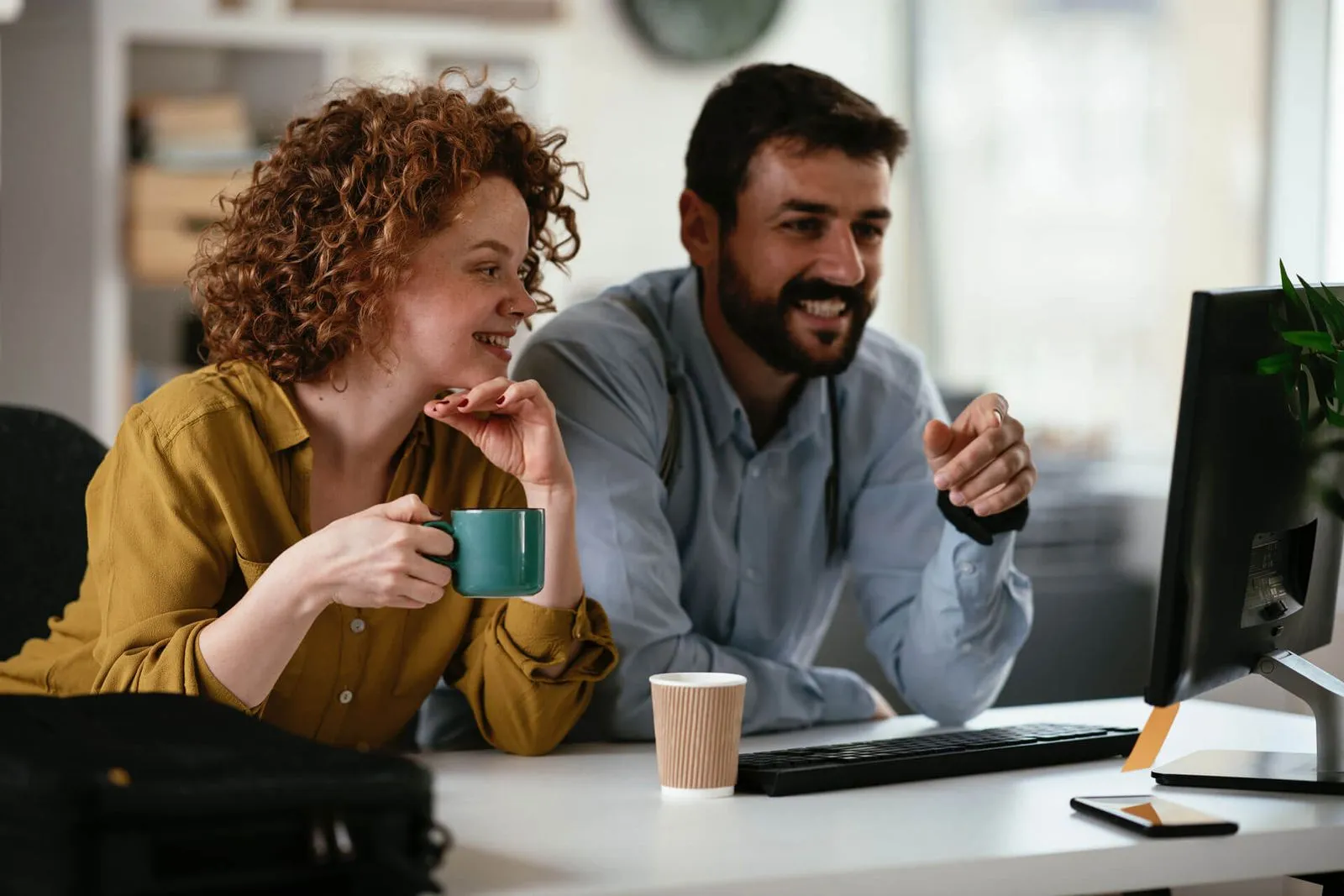 Office colleagues, a man and woman, seated at a desk with a cup of coffee.
