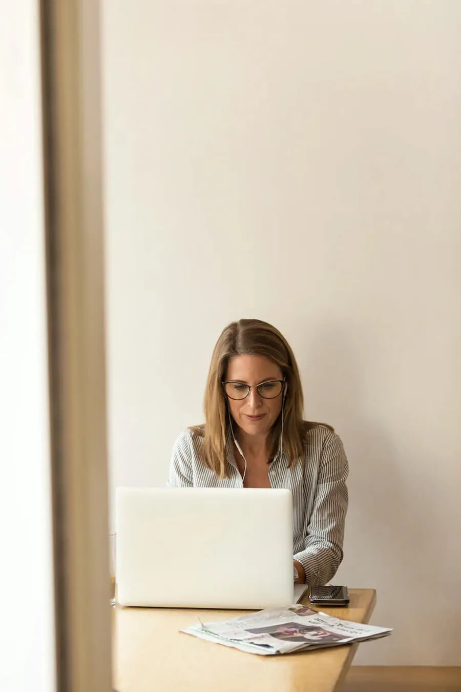 A professional woman wearing glasses is seated at a desk in an office, diligently working on her laptop.
