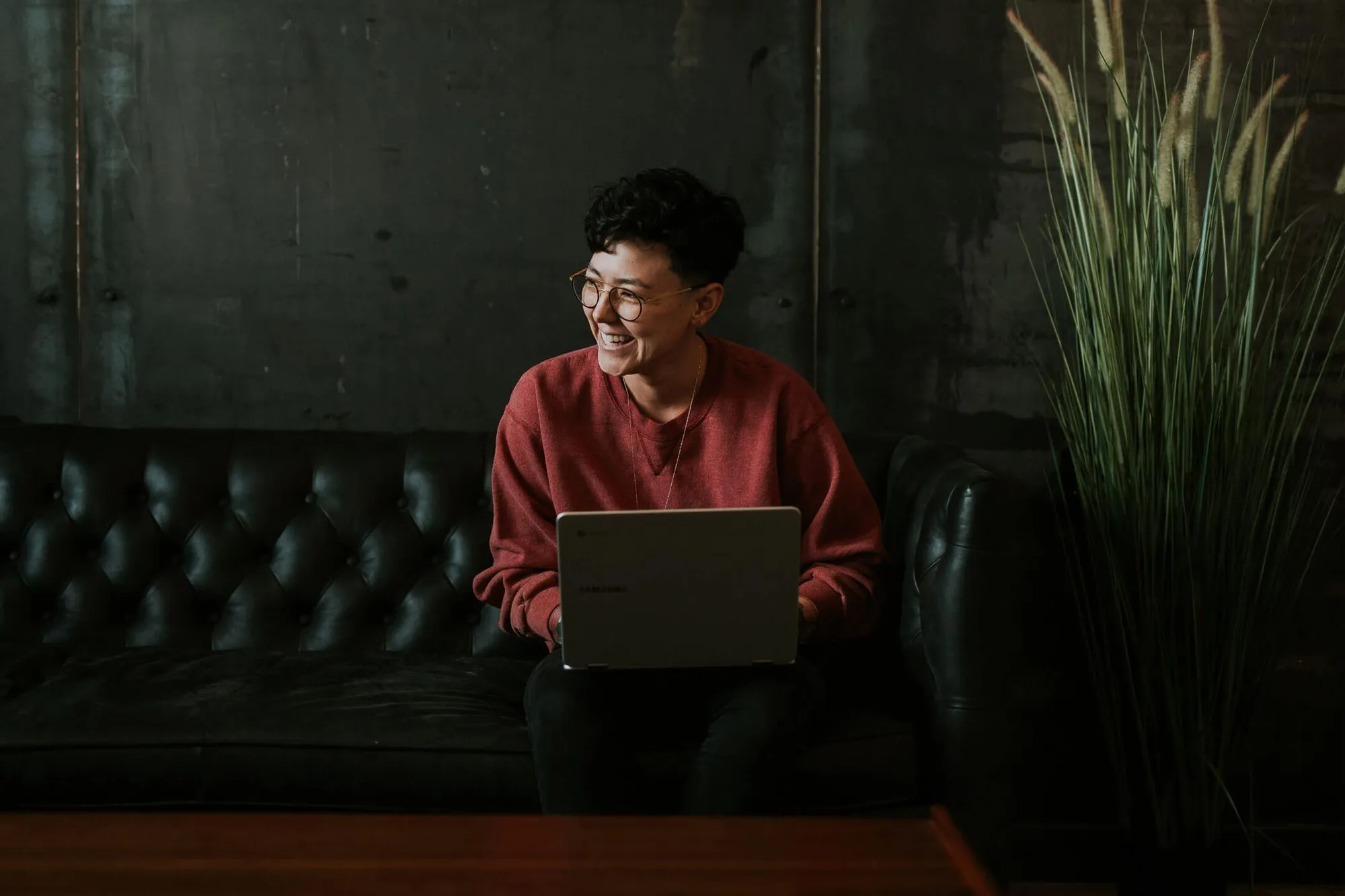 A woman smiling while working on a laptop, sitting comfortably on a couch.