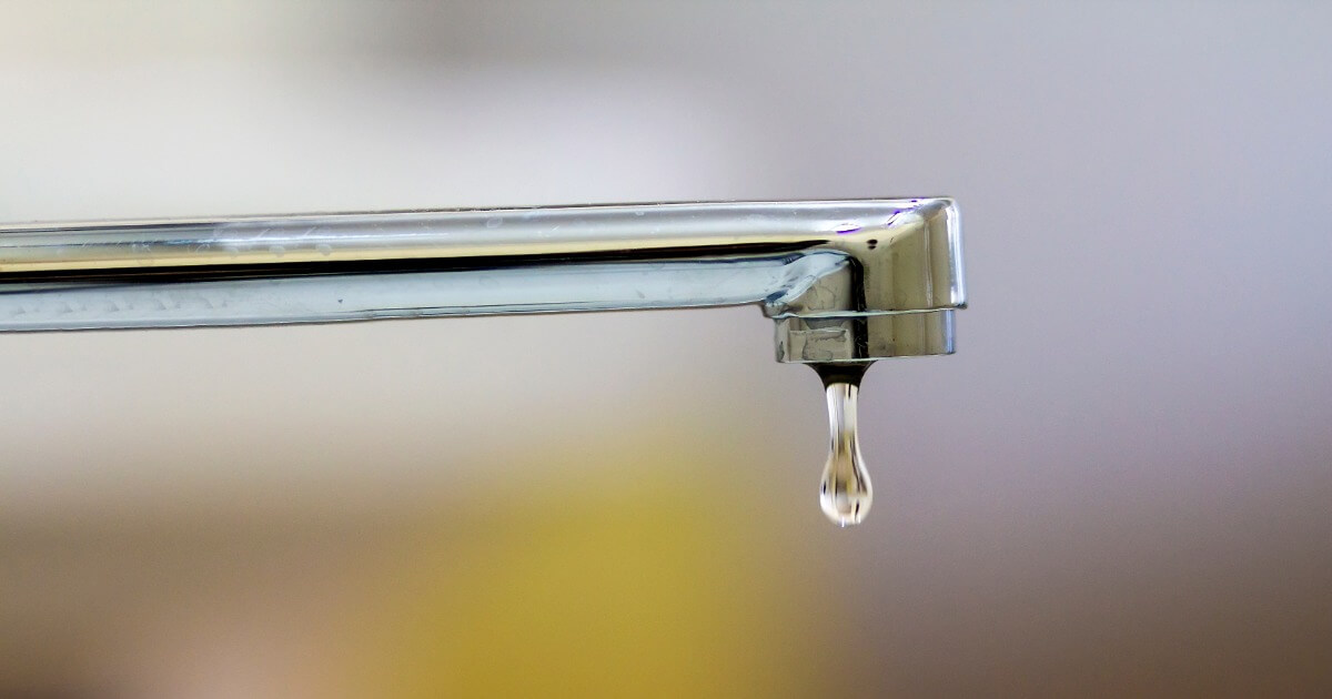 Leaking faucet with a single water droplet, highlighting water conservation and plumbing issues.