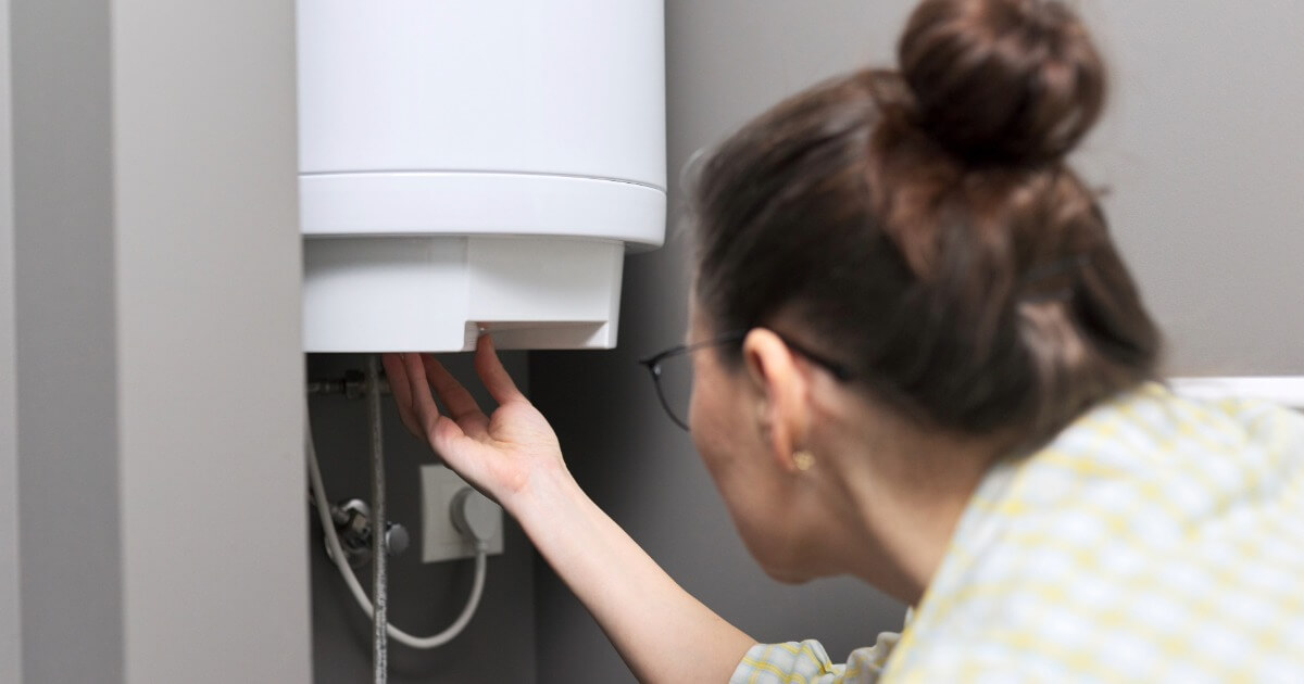 Woman inspecting a white water heater, checking connections in a utility room.