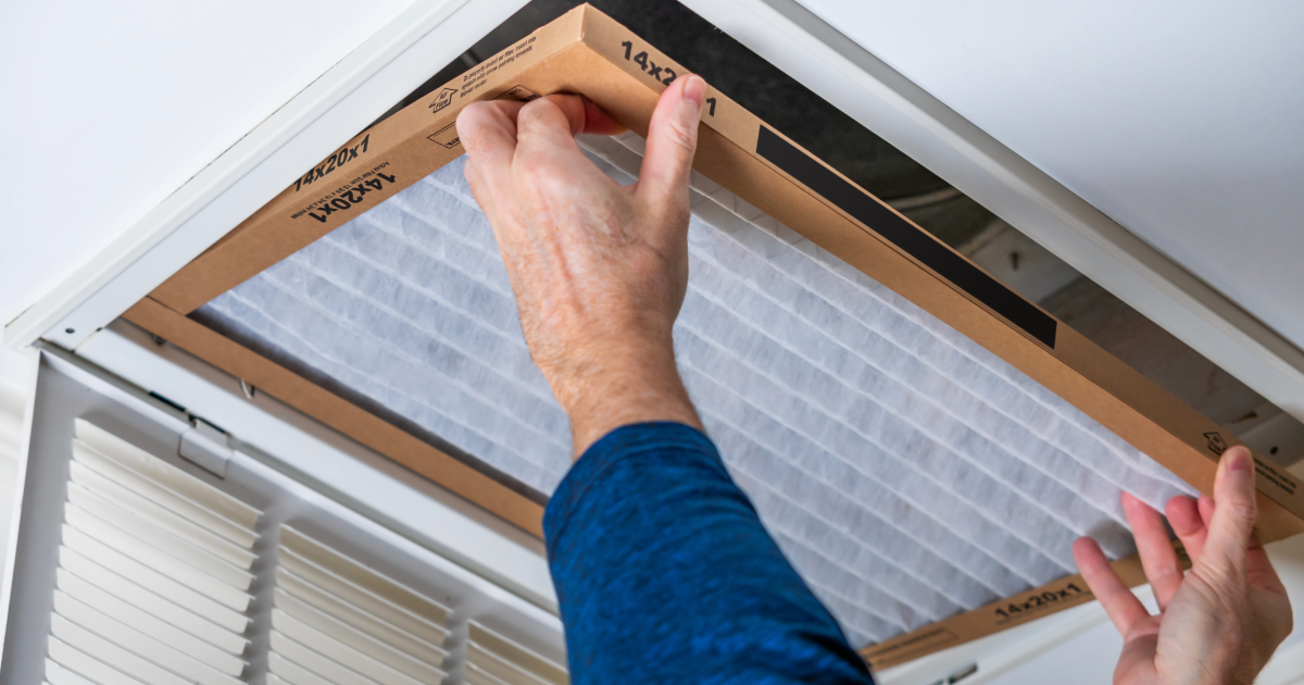 Man replacing dirty HVAC air filter in ceiling vent.