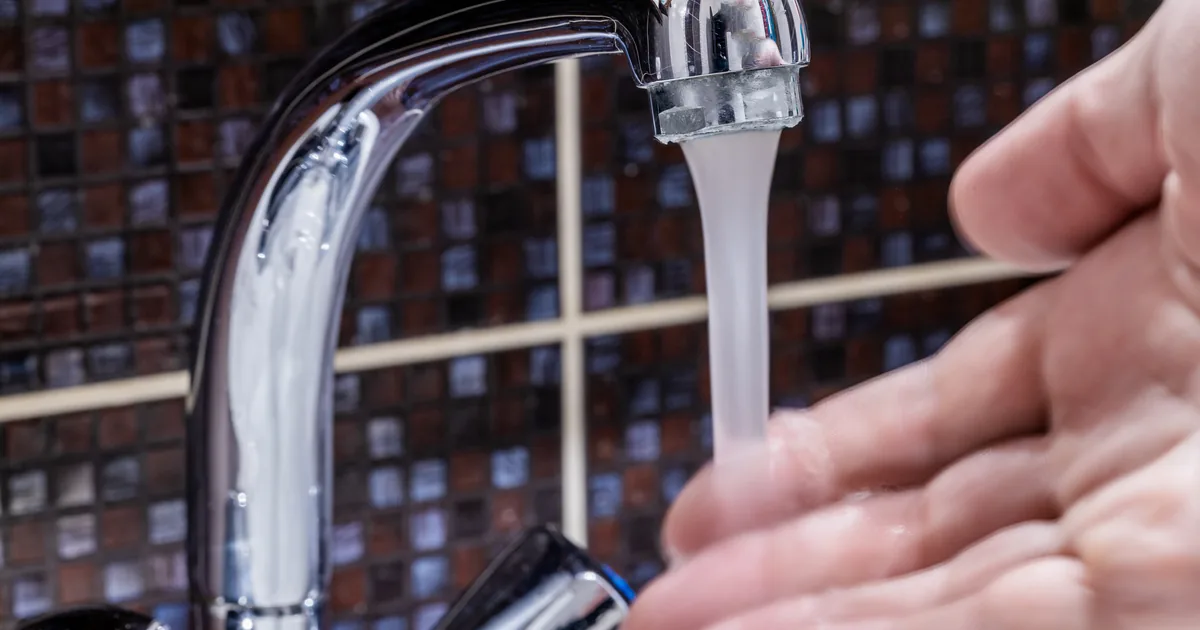Hand held under a thin stream of water from a chrome bathroom faucet with low water pressure