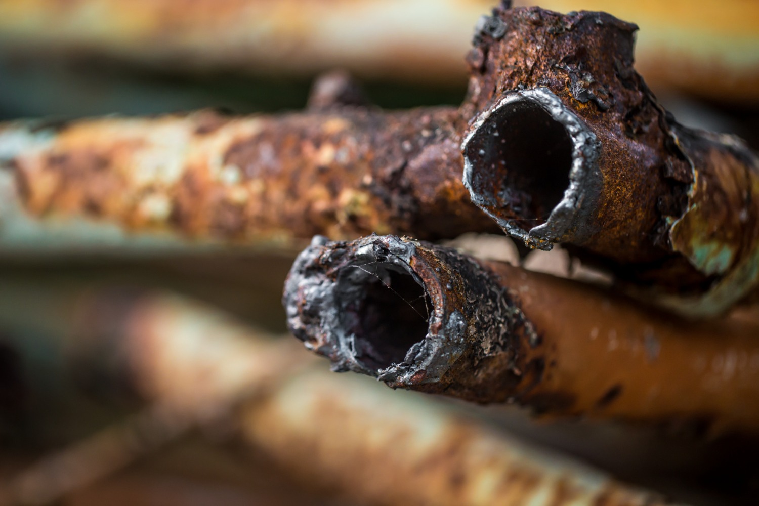 A close-up view of several old, heavily rusted, and corroded metal pipes stacked together.