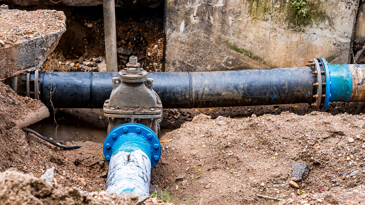  An excavation site revealing large underground utility pipes with blue flanged connections and a central valve in a dirt trench.