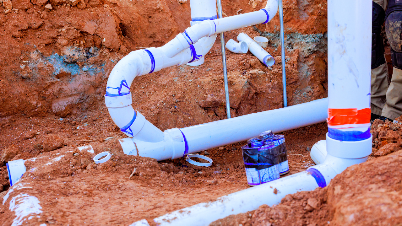 White PVC plumbing pipes with blue primer and purple cement in an excavation trench during installation or repair.