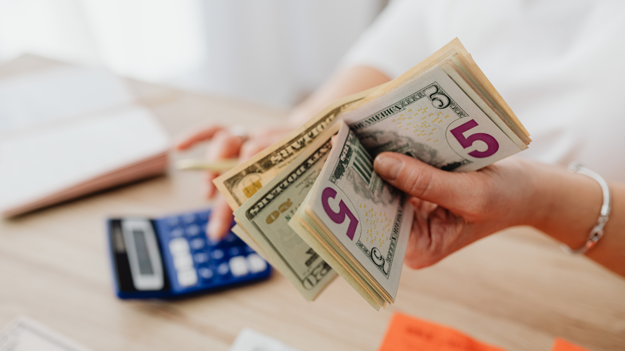 Close-up of a person holding cash and using a calculator to plan home plumbing and HVAC service costs.