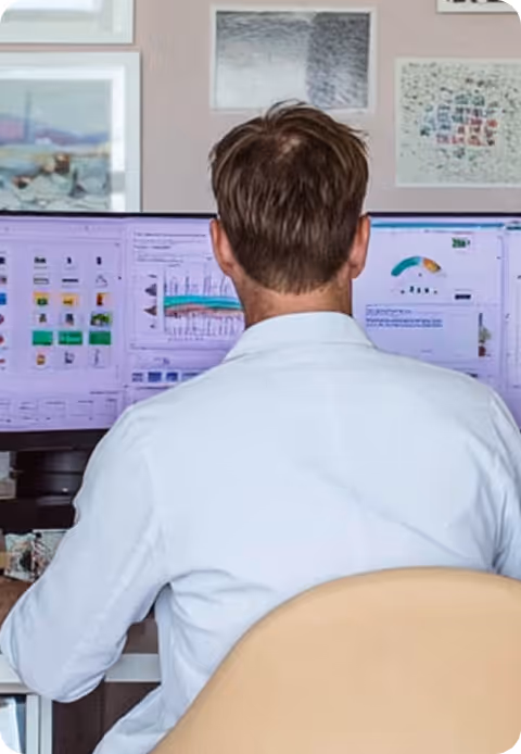 Homme vu de dos, travaillant devant deux écrans d'ordinateur affichant des graphiques et données.