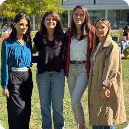 Quatre femmes debout ensemble sur une pelouse verte devant un bâtiment moderne par une journée ensoleillée.